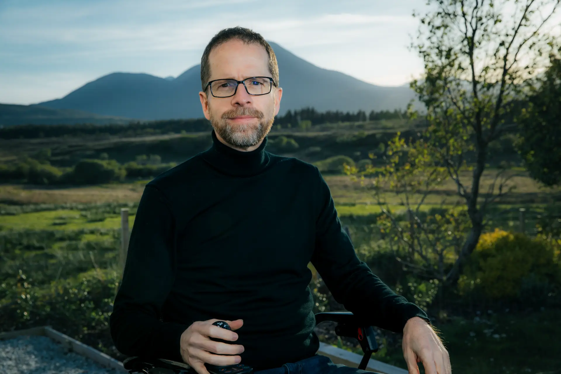 Matthew Savage seated outdoors on the Isle of Skye, mountains behind him