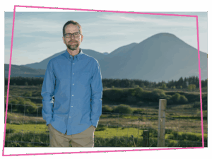 Matthew in a blue shirt stood in front of a mountain